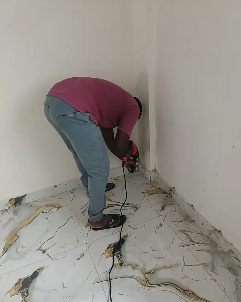 Technician drilling along the base of a wall in a marble-floored room