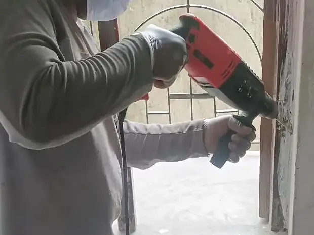 Technician in mask and cap drilling beside an arched window during termite treatment of a heritage villa